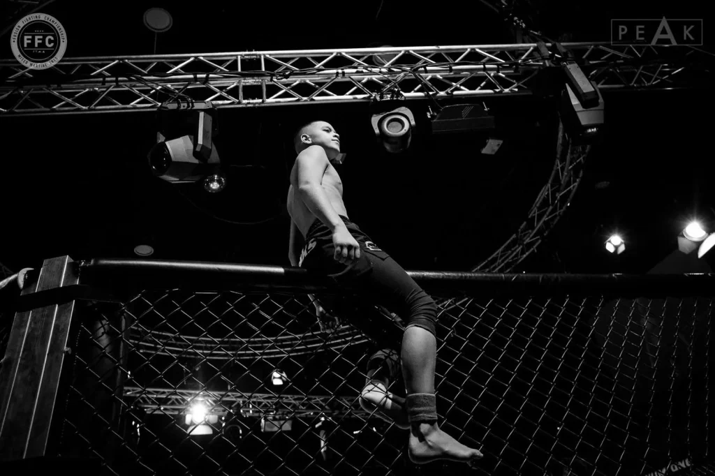 Mikail Tamoz sitting atop the MMA cage wall under arena lights