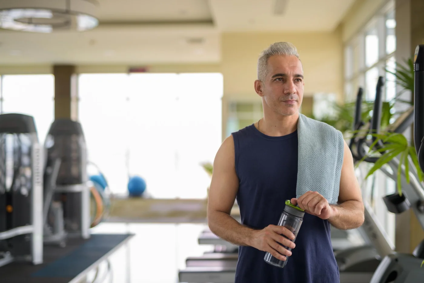 Man with gray hair at the gym, holding a water bottle and towel.