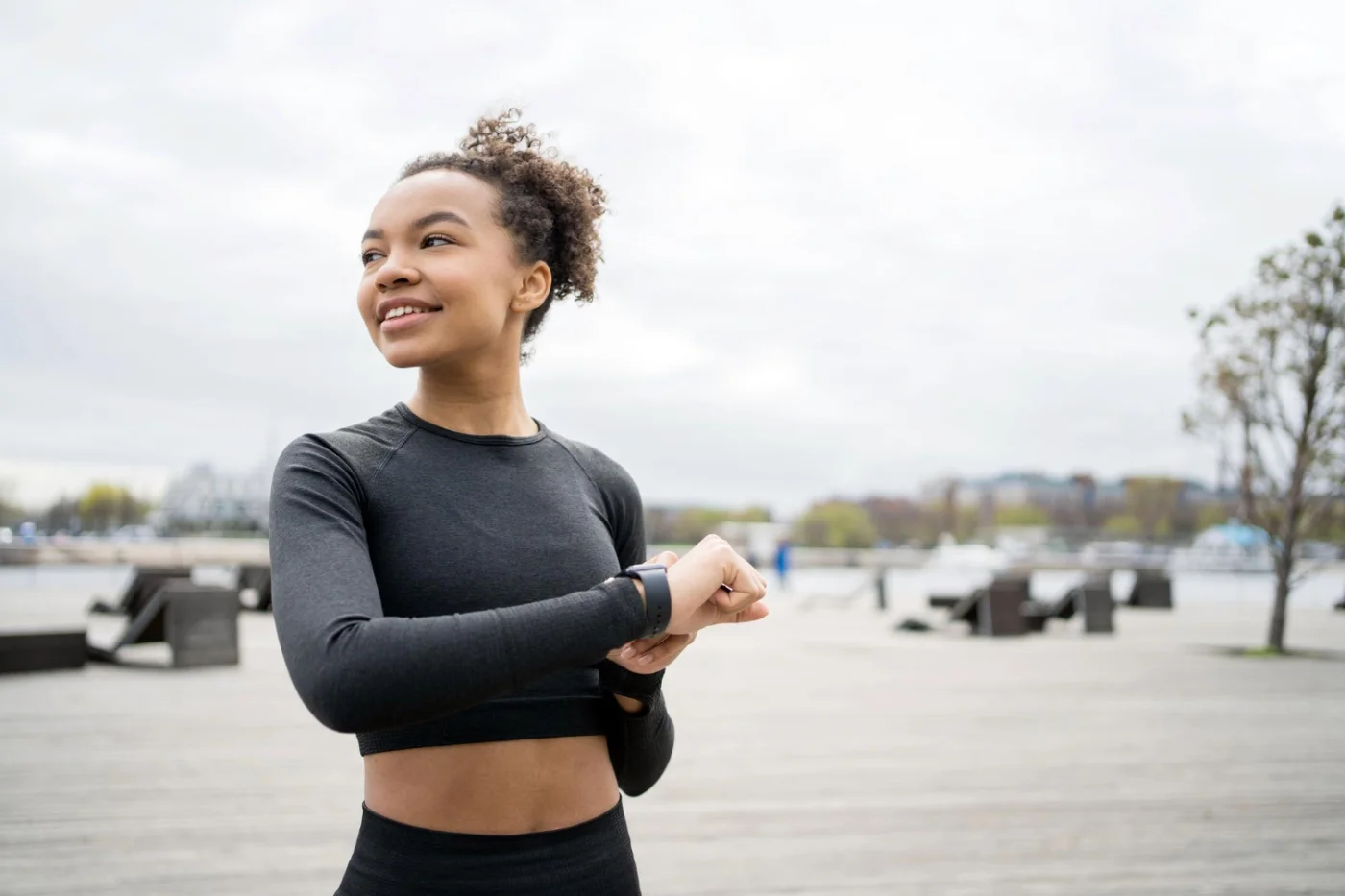 Woman in athletic wear checking smartwatch, outdoors with urban background.
