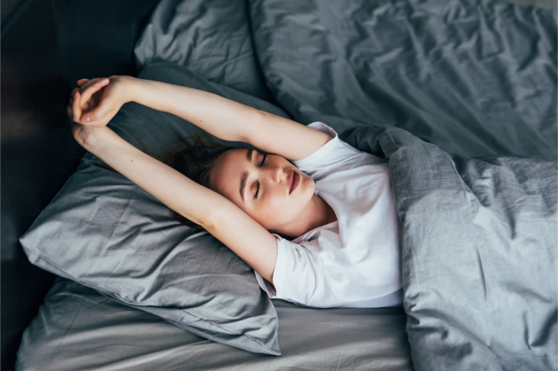 Woman experiencing insomnia lying awake in bed with grey bedding