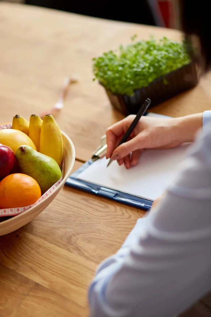 nutritionist-dietitian-woman-writing-diet-plan-with-healthy-vegetables-fruits-healthcare-diet-concept-female-nutritionist-with-fruits-working-her-desk-workplace