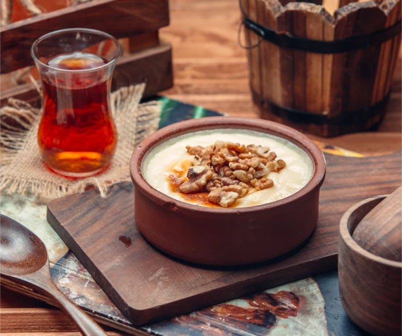 Traditional Turkish sütlaç rice pudding served in a clay bowl with walnuts and honey, paired with a glass of Turkish tea.