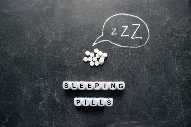 White supplement tablets with letter tiles spelling sleeping pills and ZZZ sleep bubble on chalkboard