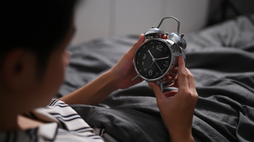 young-man-sitting-bed-turning-off-alarm-clock